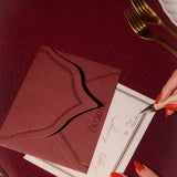 Red envelope and card on a red tablecloth with a hand holding a fork.