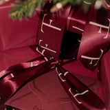 Gift wrapped in red paper with a bow, featuring a brand logo, on a blurred background.