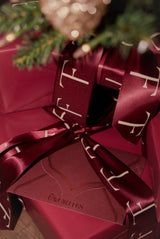 Gift wrapped in red paper with a bow, featuring a brand logo, on a blurred background.