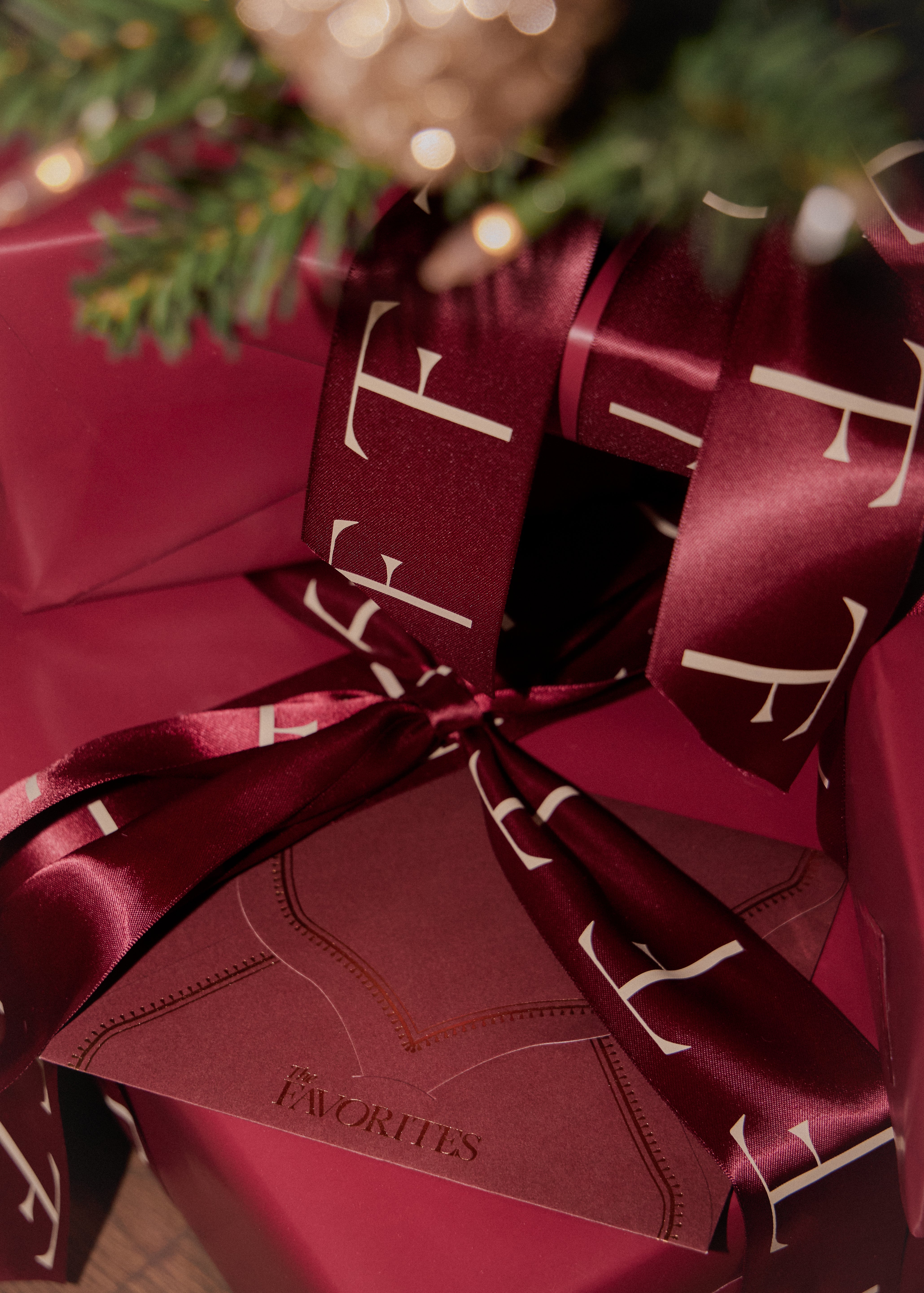 Gift wrapped in red paper with a bow, featuring a brand logo, on a blurred background.
