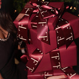 Red gift box with a bow, held by a person in front of a blurred Christmas tree.